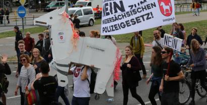 Ausschnitt einer Demo mit einem Pferd gebastelt aus Karton und einem Banner mit der Aufschrift: „Nein zum neuen niedersächsischen Polizeigesetz“.