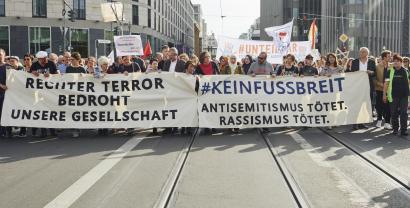 Viele Menschen auf einer Demo mit zwei Transparenten. Transparent 1: „Rechter Terror bedrohnt unsere Gesellschaft“; Transparent 2: „#KEINFUSSBREIT Antisemitismus tötet. Rassimus tötet.“