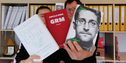 Zwei Personen halten drei Bücher Richtung Kamera: Digitale Ethik, GRM und Edward Snowden