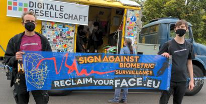Zwei Menschen halten ein Reclaim Your Face Banner hoch und stehen vor einem Lautsprecherwagen bei der unteilbar-Demo in Berlin 2021.