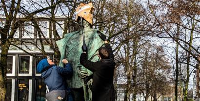 Zwei Aktivist.innen setzen einer Statue eine Papiertüte auf den Kopf