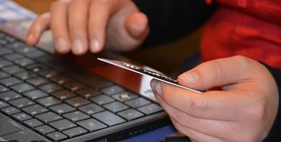 Hände, die Kreditkarte halten und Tastatur im Hintergrund.