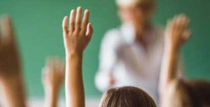 Aufzeigende Hände vor einer Tafel und einem Lehrer