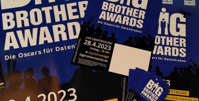 Verschiedene Werbeflyer und -plakate für die BigBrotherAwards 2023 auf einem Haufen drapiert.