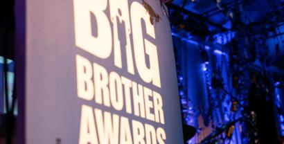 Im Vordergrund ein Banner mit der Aufschrift Big Brother Awards, im Hintergrund sphärische blaue Bühnenbeleuchtung