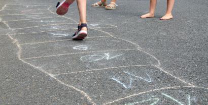 Kinder spielen und hüpfen über mit Kreide gemalte Quadrate.
