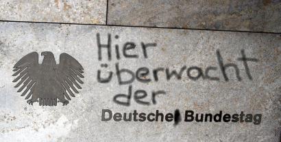 Hauswand mit dem Bundesadler und „Deutscher Bundestag“. Darüber nachträglich hinzugefügt: „Hier überwacht der“.