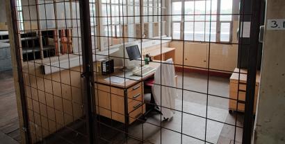 Ein Computer auf einem Schreibtisch in einer Art Zelle hinter Gittern.