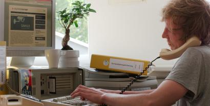 Ein Digitalcourage-Mitarbeiter vor einem alten PC mit Schnurtelefon am Ohr.