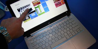 Detailaufnahmer einer Hand, die auf einen Laptop-Bildschirm zeigt, wo eine Seite zum Online-Einkauf geöffnet ist.