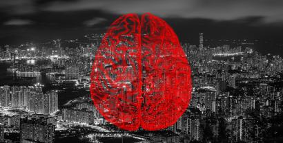 Collage: Im Hintergrund eine Großstadt bei Nacht (schwarz-weiß). Darüber eine Grafik eines Gehirns im Querschnitt (rot).