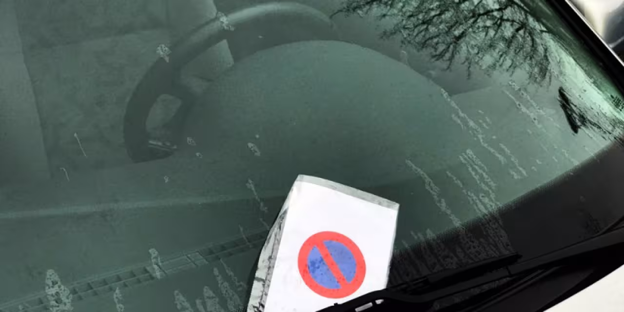 Ein Strafzettel, der hinter einem Scheibenwischer hängt.