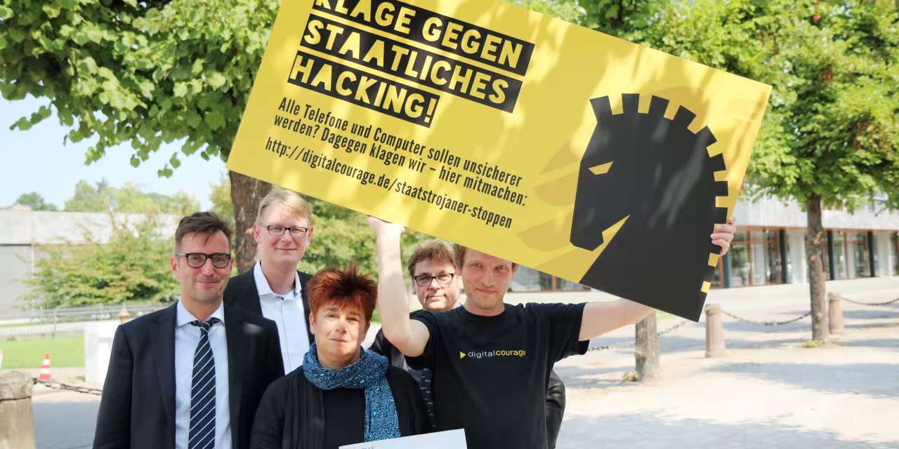 Rena Tangens und padeluun mit drei weiteren Personen, wovon eine ein Schild hochält: „Klage gegen staatliches Hacking“.