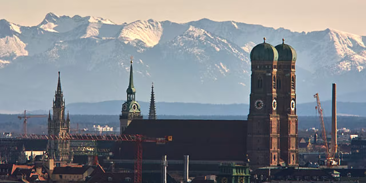 Frauenkirche in München aus der Entfernung. Im Hintergrund die Alpen.