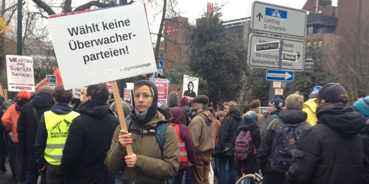 Eine Person auf einer Demo hält ein Schild in der Hand. Darauf steht: „Wählt keine Überwacherparteien“.