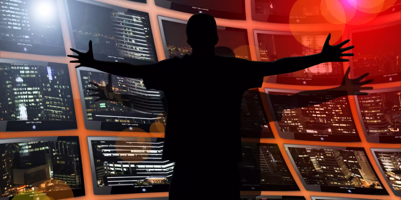 Eine Silhouette einer Person die vor einer Vielzahl von Monitoren steht.
