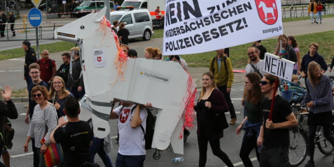 Ausschnitt einer Demo mit einem Pferd gebastelt aus Karton und einem Banner mit der Aufschrift: „Nein zum neuen niedersächsischen Polizeigesetz“.