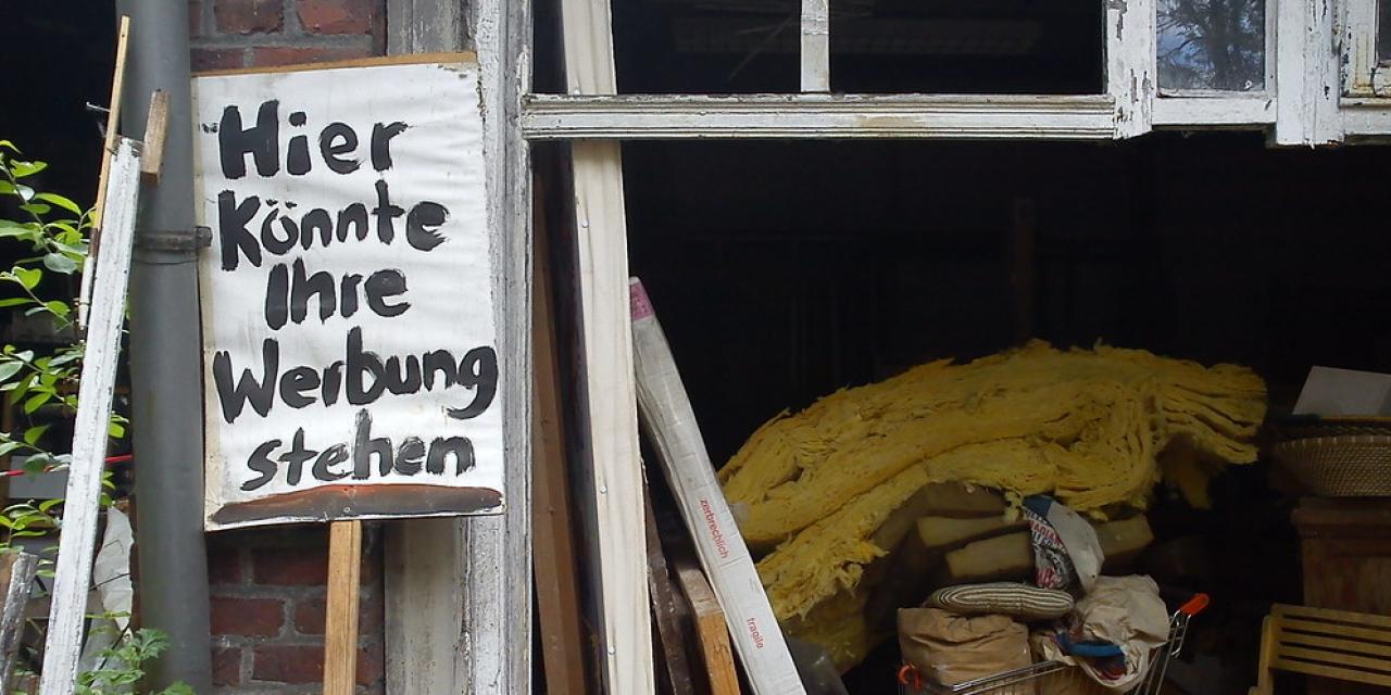 Eine vollgestellte Garage. Davor ein Schild mit dem Schriftzug: „Hier könnte ihre Werbung stehen“.