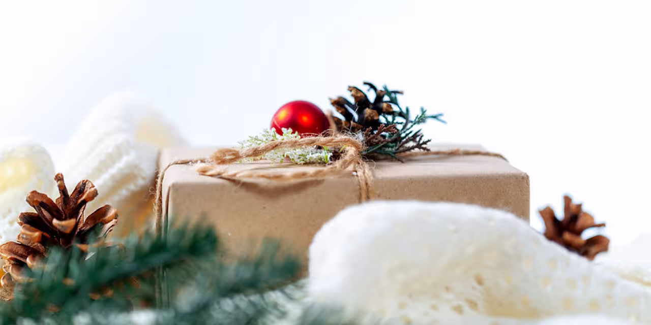Ein in Paketpapier eingepacktes Geschenk mit weihnachtlicher Dekoration drumherum.