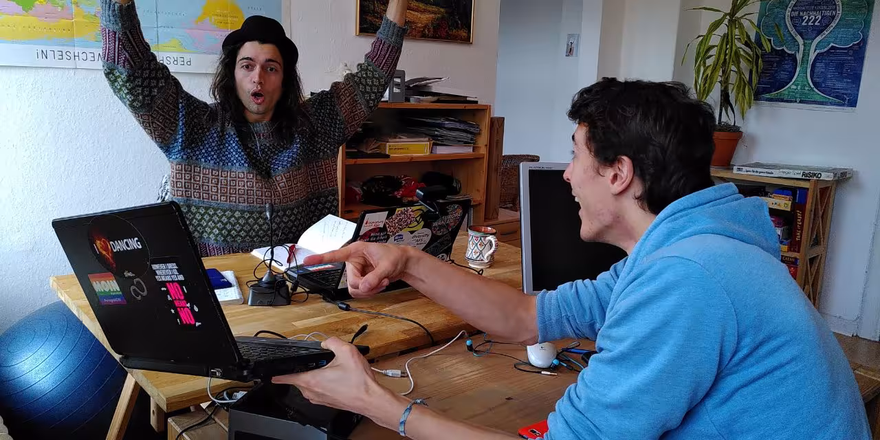 Trainer.innen Adrian und Robin Grimm (Die Gebrüder Grimm) jubelnd-freudig an einem Laptop.