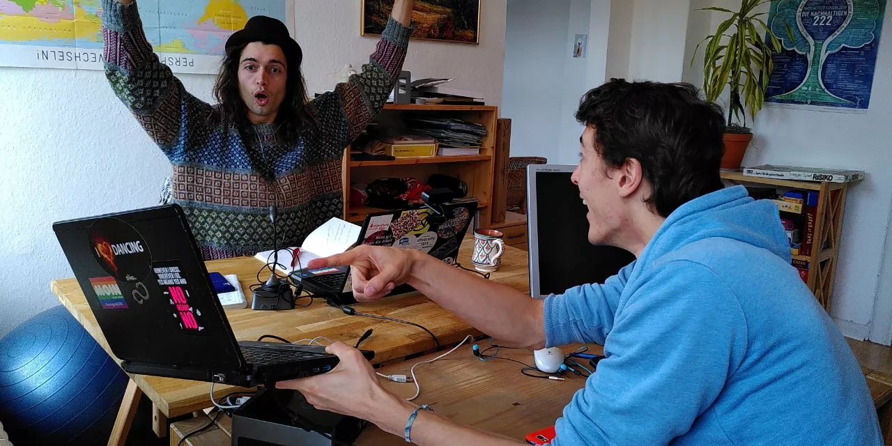 Trainer.innen Adrian und Robin Grimm (Die Gebrüder Grimm) jubelnd-freudig an einem Laptop.
