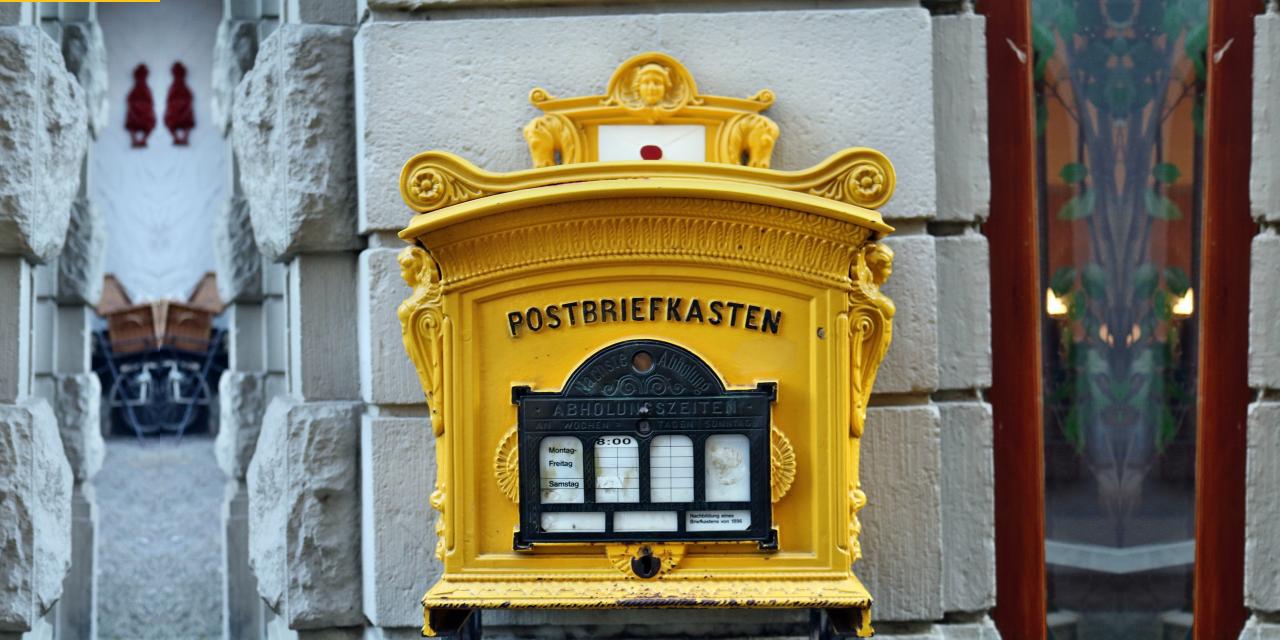 Ein gelber Postbriefkasten an einer Hauswand.