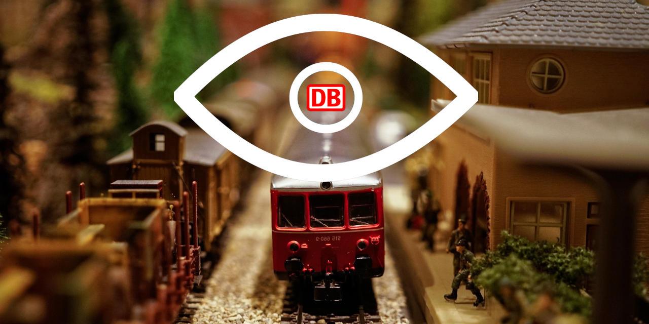 Ein großes Auge, dessen Pupille aus dem Logo der Deutschen Bahn AG besteht, überblickt einen Miniaturbahnhof.