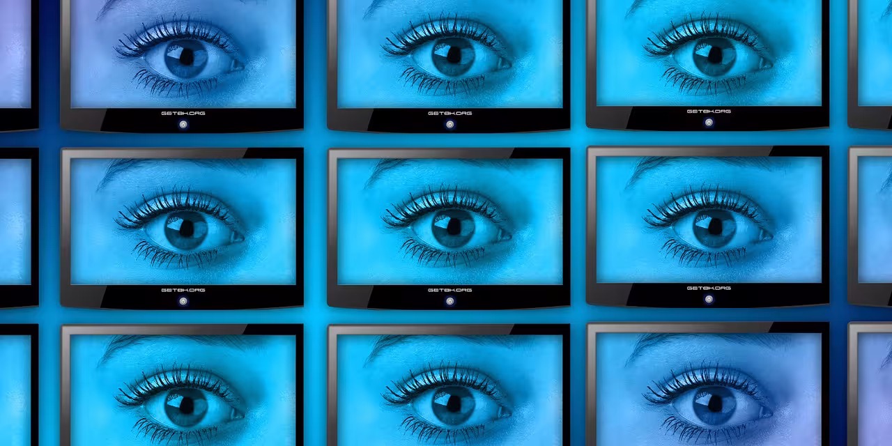Eine Wand voller Smart-TVs. Jeder Bildschirm zeigt ein großes, offenes Auge.