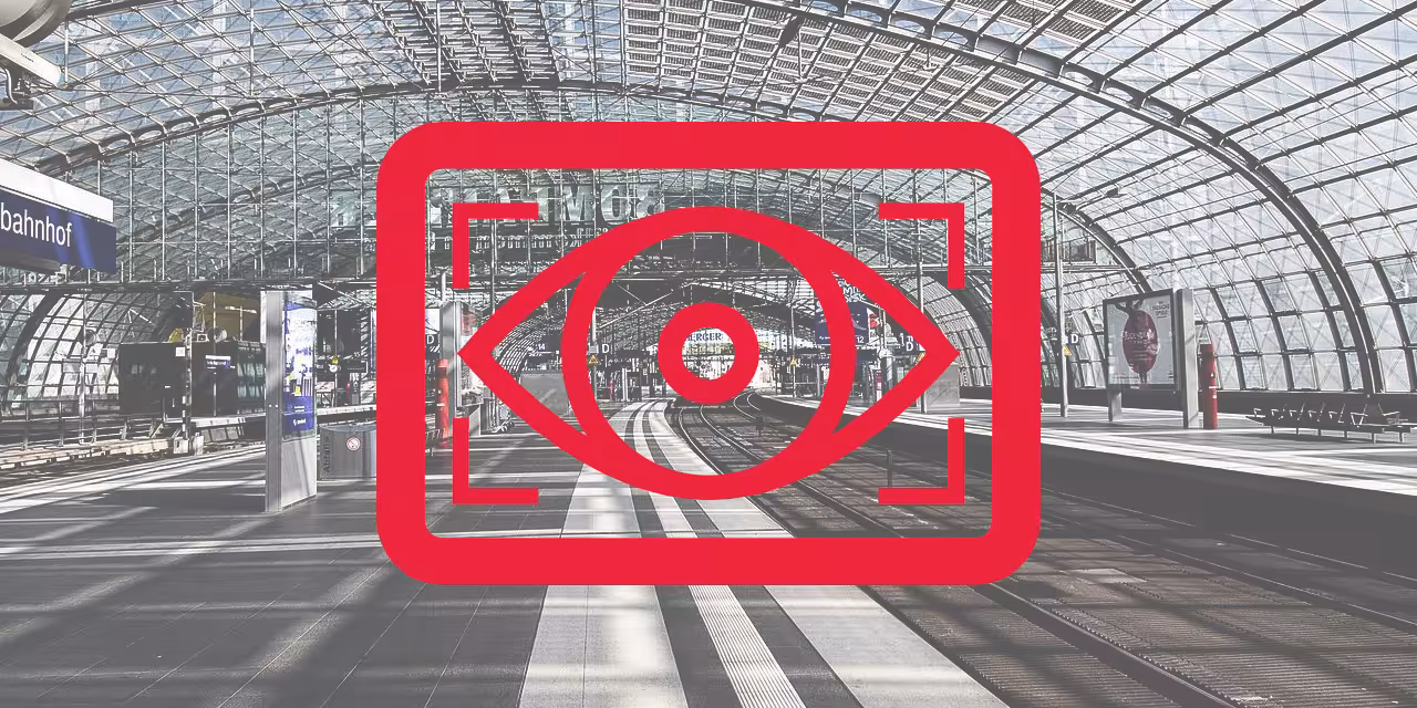 Rotes Kampagnenlogo mit einem stilisierten Auge. Im Hintergrund eine große Bahnhofshalle. 