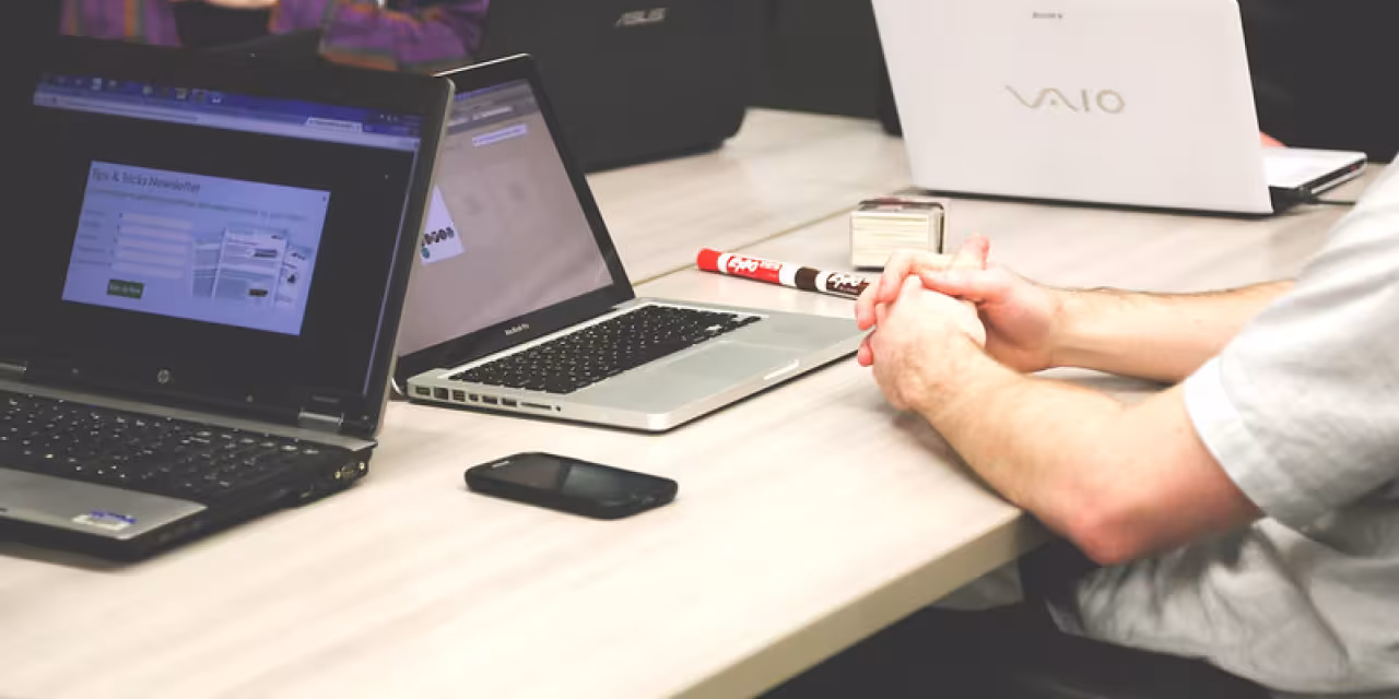 Foto von mehreren Personen, die mit ihren Laptops um einen hölzernen Tisch sitzen