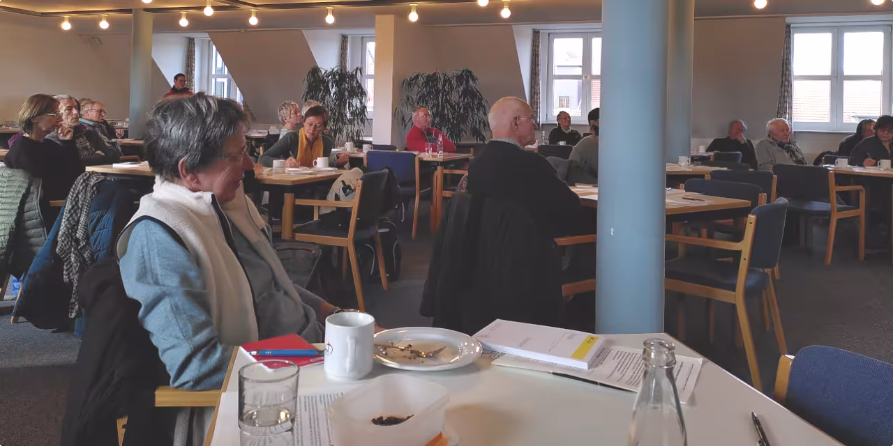 An meherern Tischen sitzen Leute und schauen nach vorne, auf den Tischen stehen Teller mit Kuchenkrümeln und Kaffeetassen