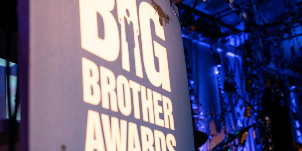 Im Vordergrund ein Banner mit der Aufschrift Big Brother Awards, im Hintergrund sphärische blaue Bühnenbeleuchtung