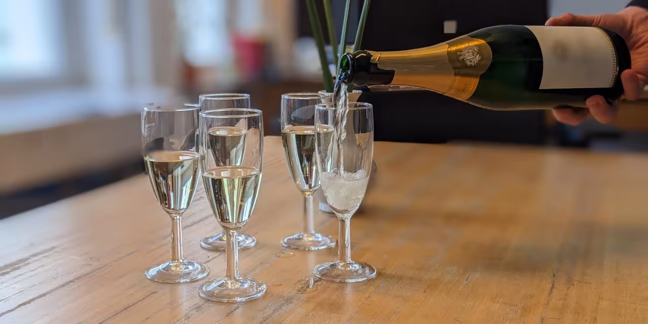 Mehrere Sektgläser stehen gefüllt auf einem Tisch. Das letzte verbleibende Sektglas wird gerade mit einer Sektflasche befüllt.