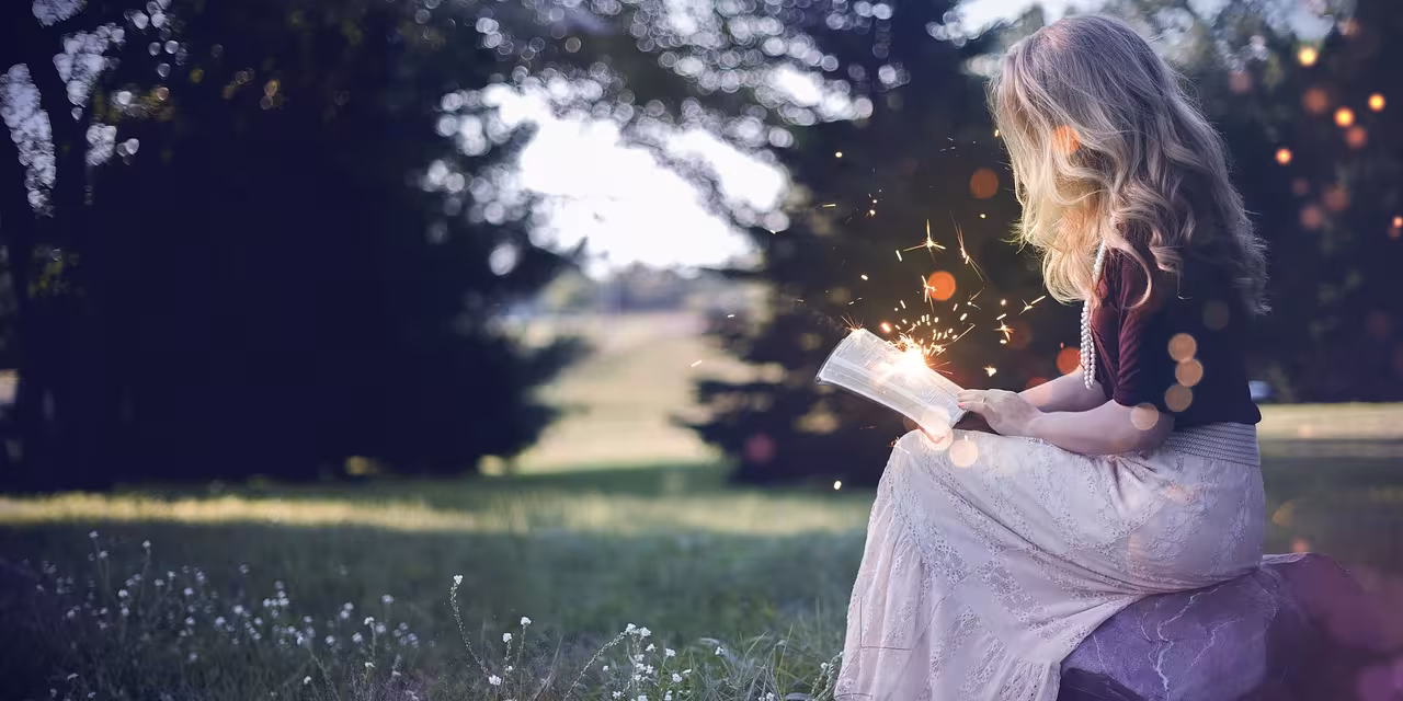 Ein Mächen sitzt auf einer Wiese und liest ein Buch, aus dem Funken sprühen