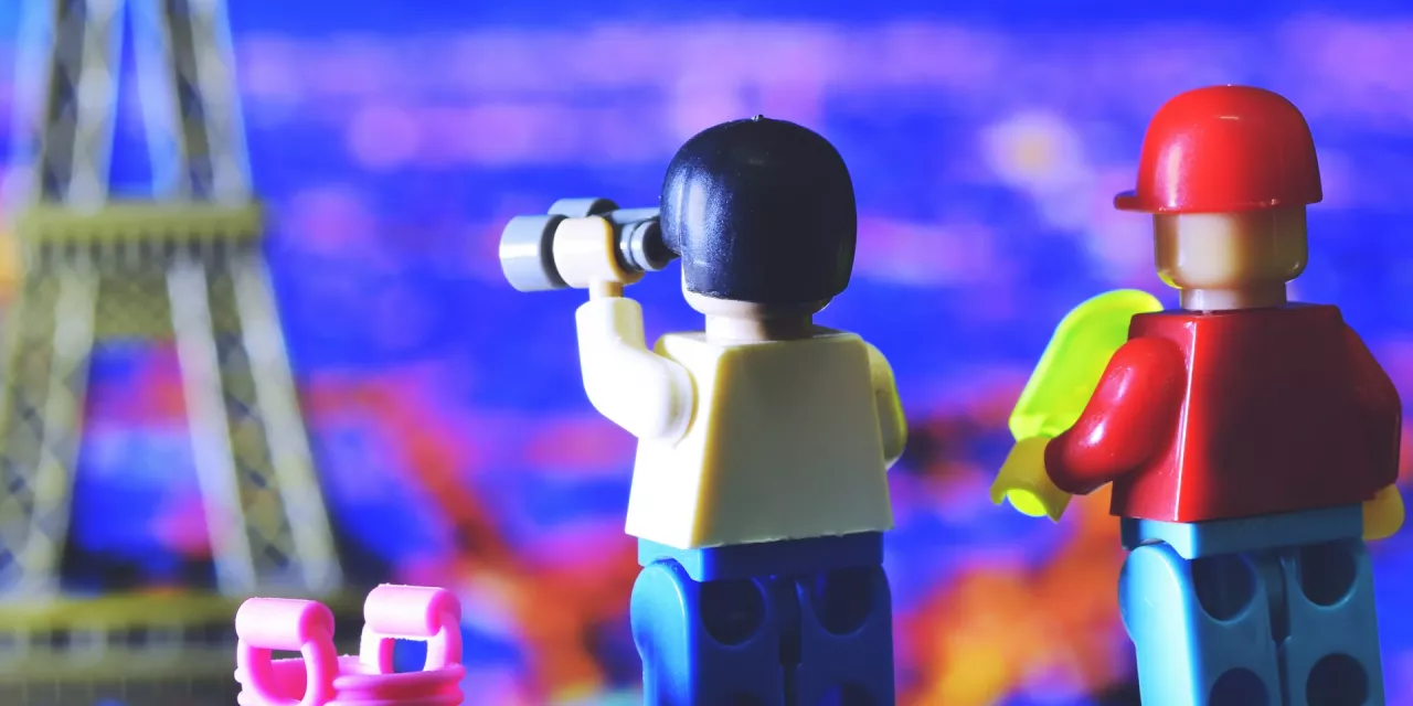 Zwei Lego-Figürchen. Eins blickt mit einem Fernglas in die Ferne, das andere trägt einen Bauhelm. Beide stehen direkt beieinander.