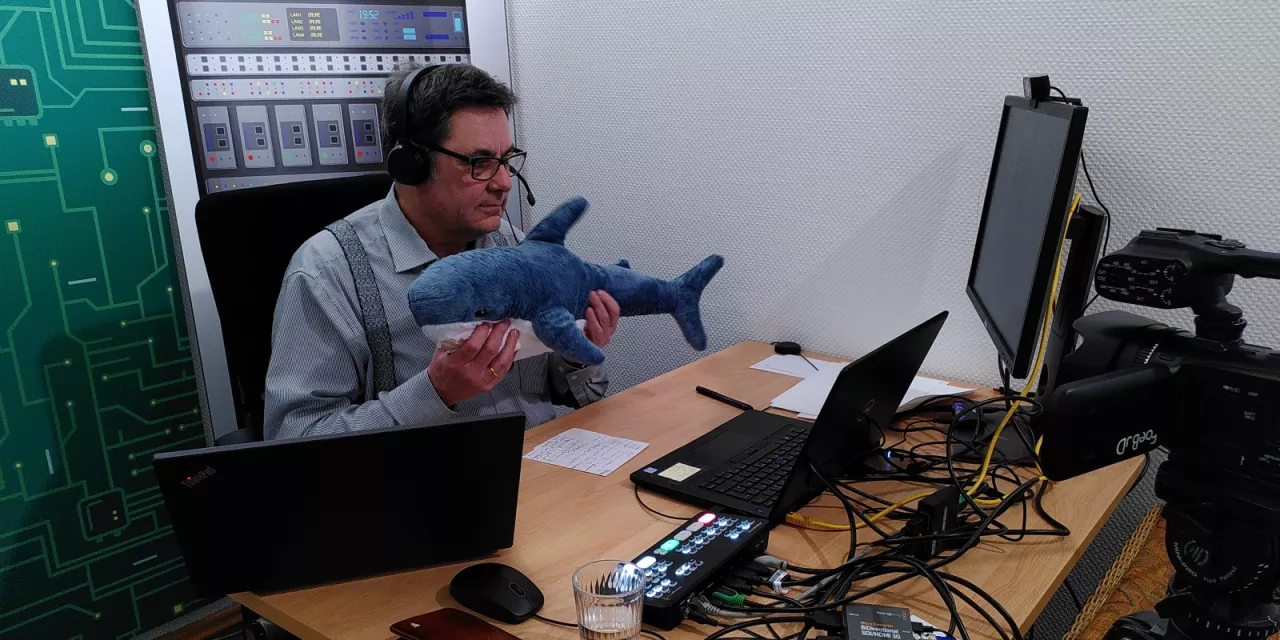 padeluun hält einen Online-Vortrag – in seinen Händen streckt er einen Plüschhai Richtung Webcam.