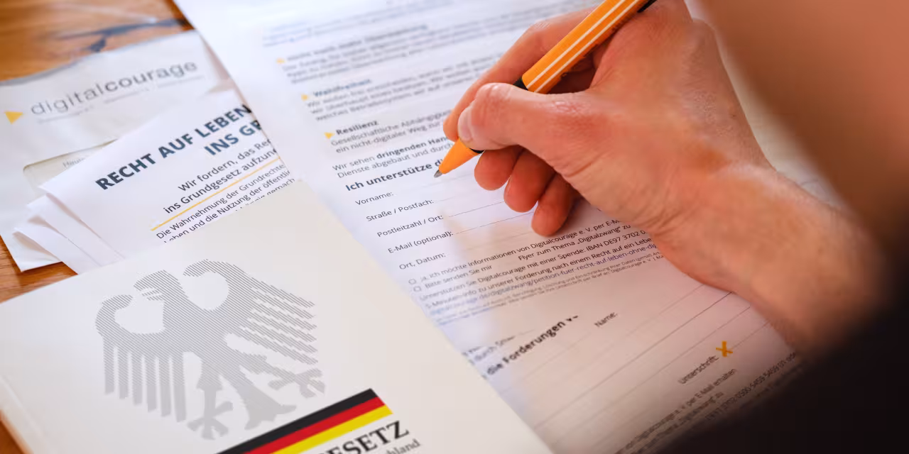 Eine Person ist dabei, die Petition zu unterzeichnen. Neben der ausgedruckten Petition liegt das Grundgesetz.