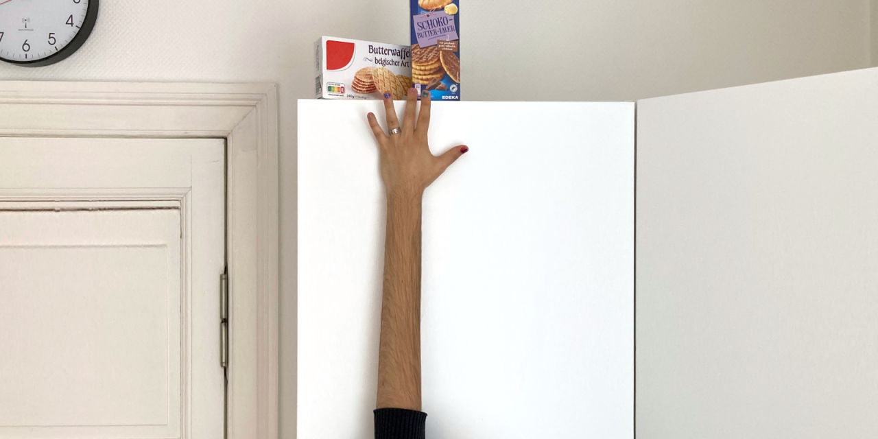 Foto eines Arms, der mit Hilfe eines Grafikprogramms künstlich verlängert wurde, um an Kekse zu kommen, die auf einem hohen Schrank stehen.