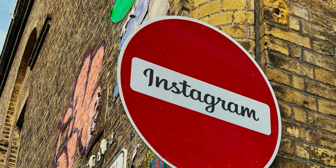 Detailaufnahme des Straßenschildes „Keine Durchfahrt“ (roter Kreis mit weißem Querbalken). Im weißen Bereich steht: „Instagram“. Im Hintergrund eine Klinkerwand mit Graffiti.