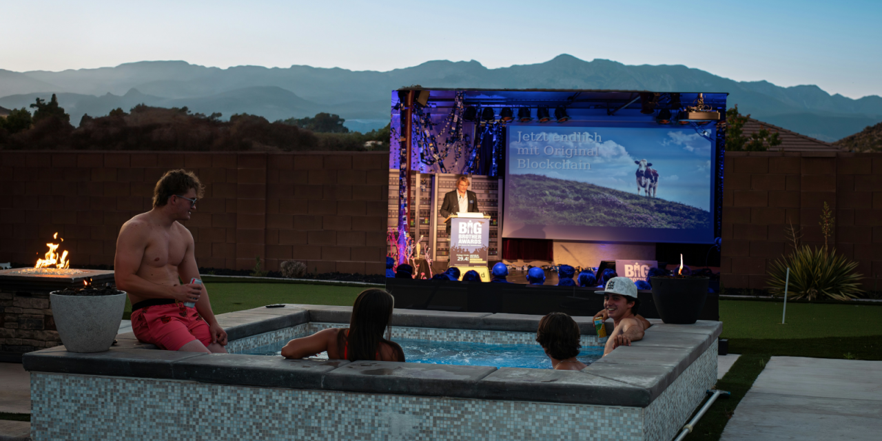 Fotomontage: Menschen in einem Whirlpool bei Dämmerung. Sie schauen auf eine Leinwand. Abgebildet ist ein Ausschnitt der BigBrotherAwards-Gala.