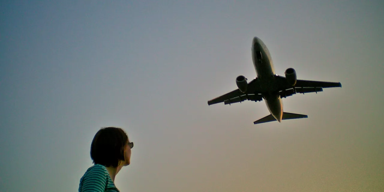 Froschperspektive: Silhouette eine Person. Darüber in der Ferne ein Flugzeug.