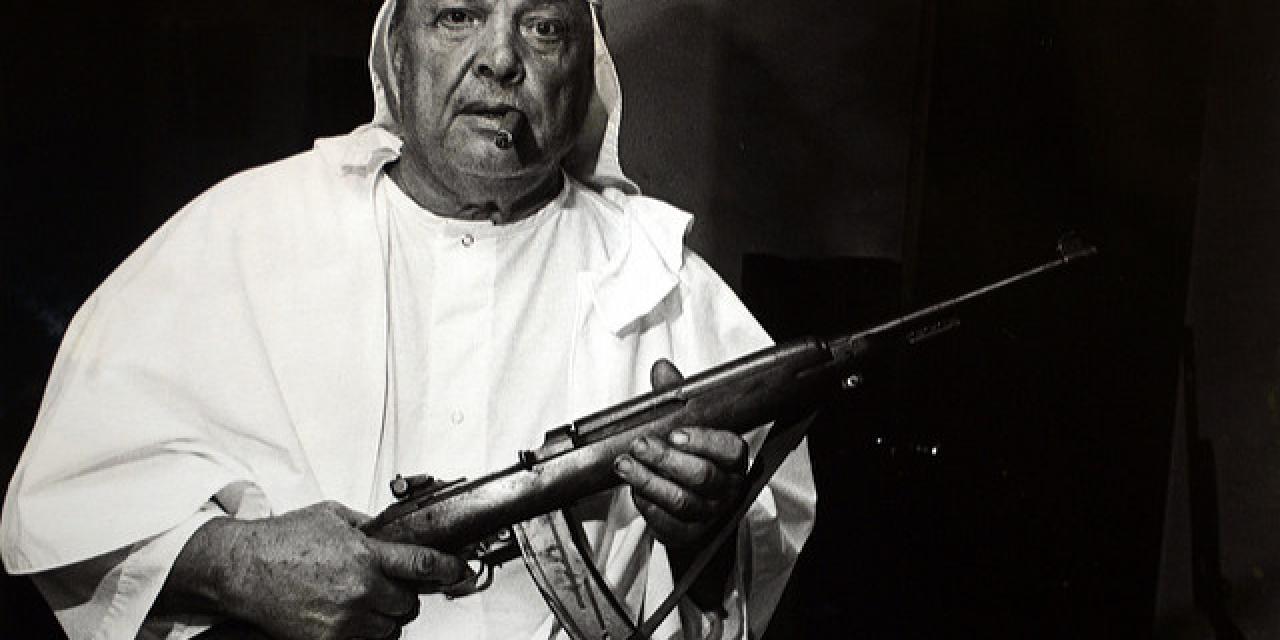 Ein Mann in einer Robe des KuKluxKlan mit einer Waffe in der Hand (schwarz-weiß).