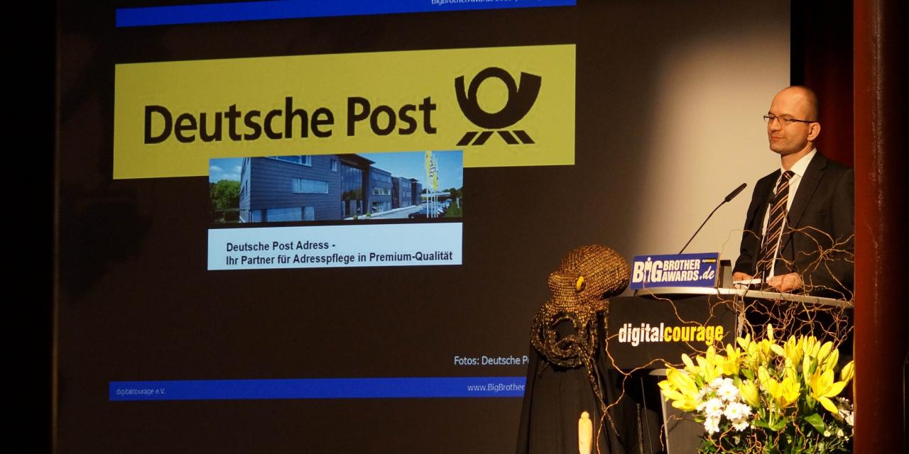 Sönke Hilbrans am Redner.innenpult der BBAs 2013. Im Hintergrund das Logo der Deutschen Post.