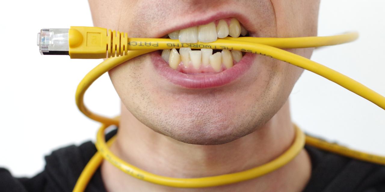 Detailaufnahme einer Person (Mundpartie), die ein gelbes Ethernet-Kabel um den Hals udn im Mund hat.