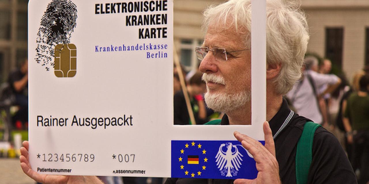 Ein Aktivist mit einer großen elektronischen Gesundheitskarte mit einem rechteckigen Loch auf der rechten Seite, wo ein Mensch durchschaut.
