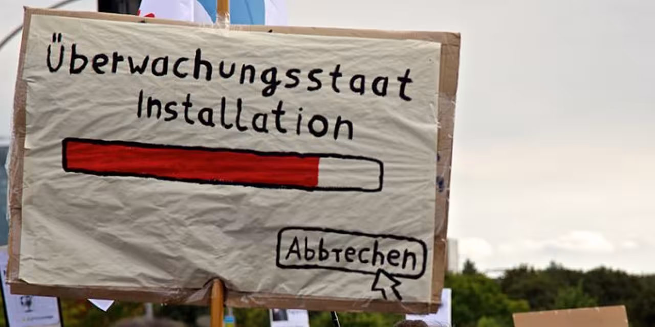 Demoschild mit einem Ladebalken und dem Text „Überwachungsstaat Installation“. Darunter ein Mauszeiger, der auf „Abbrechen“ klickt.