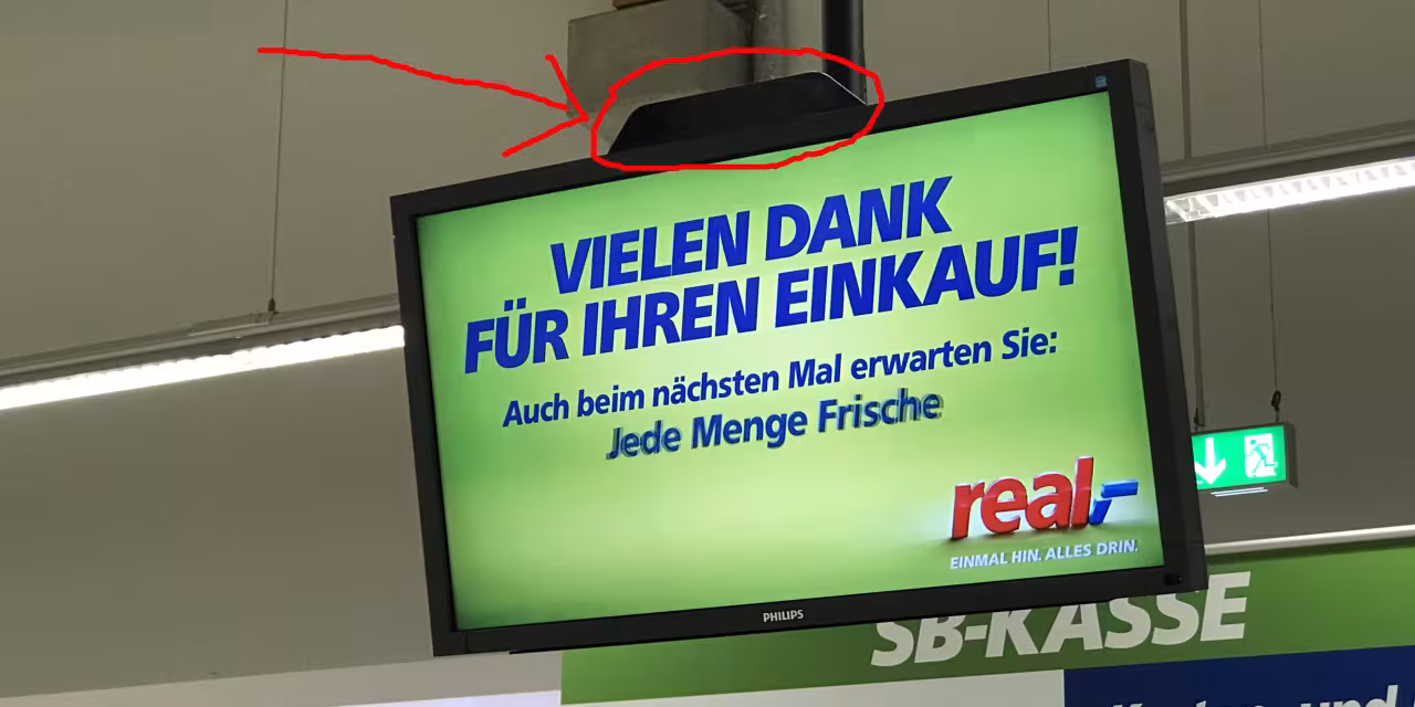 Ein Bildschirm mit einem Werbetext von real,-. Eine kleine schwarze Box am oberen Bildschirmrand ist in rot eingekreist.