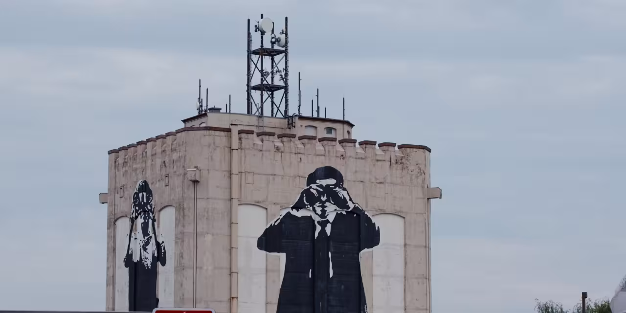 Eine Art Bunker mit Graffitis: Zwei Personen die jeweils ein Fernrohr in der Hand haben und vor die Augen halten.