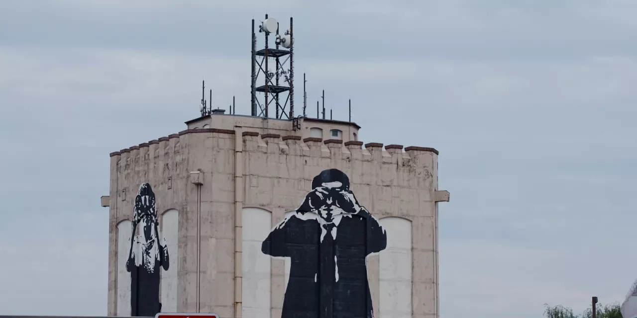 Eine Art Bunker mit Graffitis: Zwei Personen die jeweils ein Fernrohr in der Hand haben und vor die Augen halten.