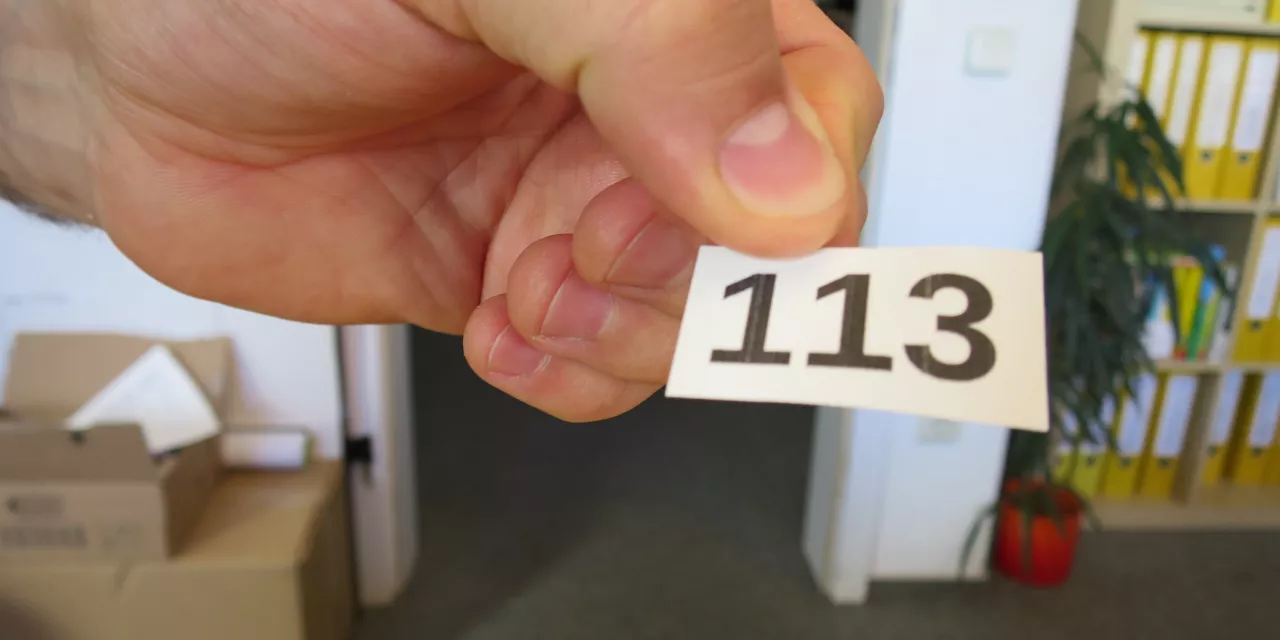 Detailaufnahmer einer Hand, die einen Zettel mit einer Zahl (113) in der Hand hält.